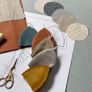 Puede incluir: Un conjunto de cinco formas de tela en varios colores, incluyendo azul verdoso, marr&oacute;n, beige, gris y amarillo. Las formas est&aacute;n dispuestas sobre una hoja de papel blanco con el texto "Set your printer settings to" impreso en ella. El papel est&aacute; sobre una estera de corte verde.