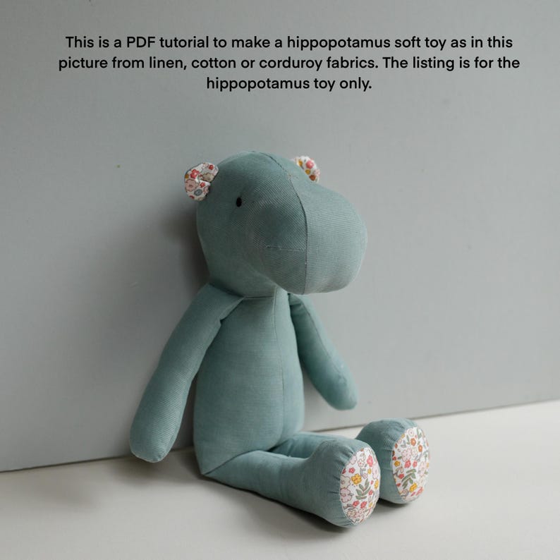 May include: A teal blue fabric hippopotamus soft toy with floral fabric accents on the ears and feet. The toy is sitting on a light gray surface.