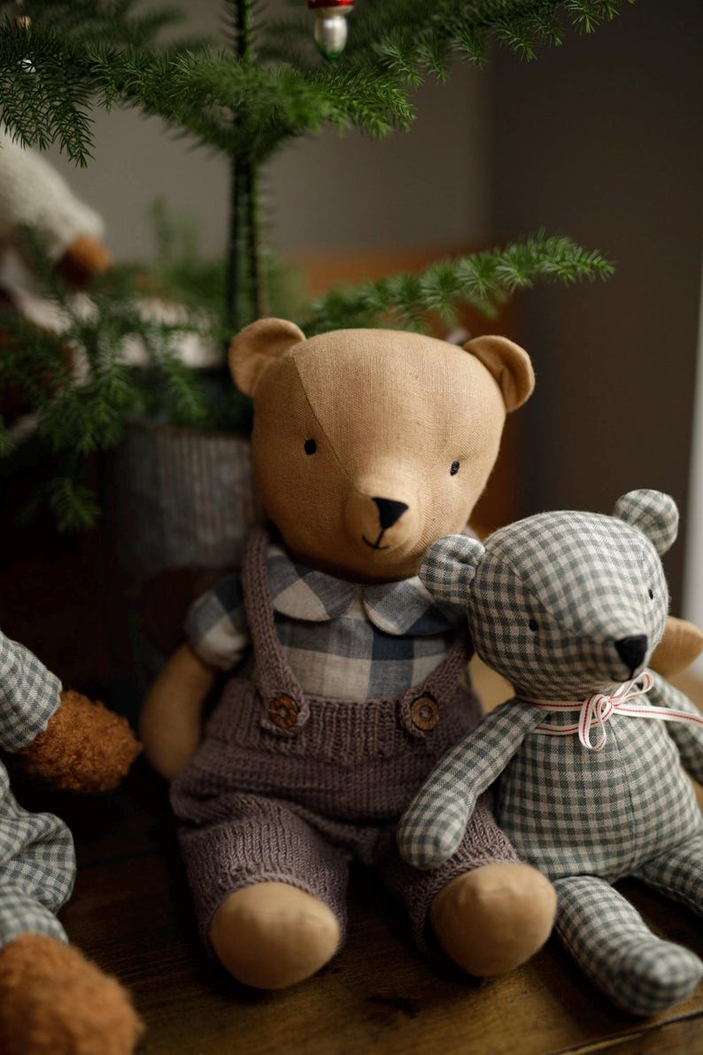 May include: Two plush teddy bears, one brown with a plaid shirt and brown overalls, and one green and white plaid bear with a pink ribbon. The bears are sitting on a wooden surface.