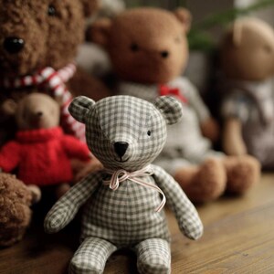 May include: A group of plush teddy bears, including a brown bear with a red and white scarf, a brown bear with a light brown and white checkered pattern, and a gray and white checkered bear with a red and white ribbon.
