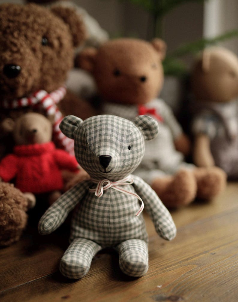 May include: A group of plush teddy bears, including a brown bear with a red and white scarf, a brown bear with a light brown and white checkered pattern, and a gray and white checkered bear with a red and white ribbon.