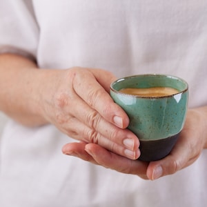 May include: A person's hands holding a green and black ceramic mug filled with coffee.