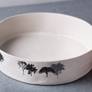 May include: White ceramic serving bowl with a black silhouette of trees around the rim.