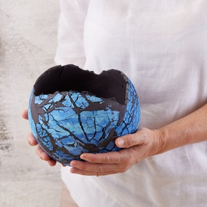 May include: A blue and black ceramic bowl with a crackled glaze. The bowl is broken in one place, revealing the black clay underneath.