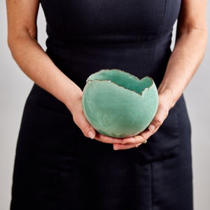 May include: A teal ceramic bowl with a rough, uneven rim. The bowl is slightly misshapen and has a rustic, handmade look.