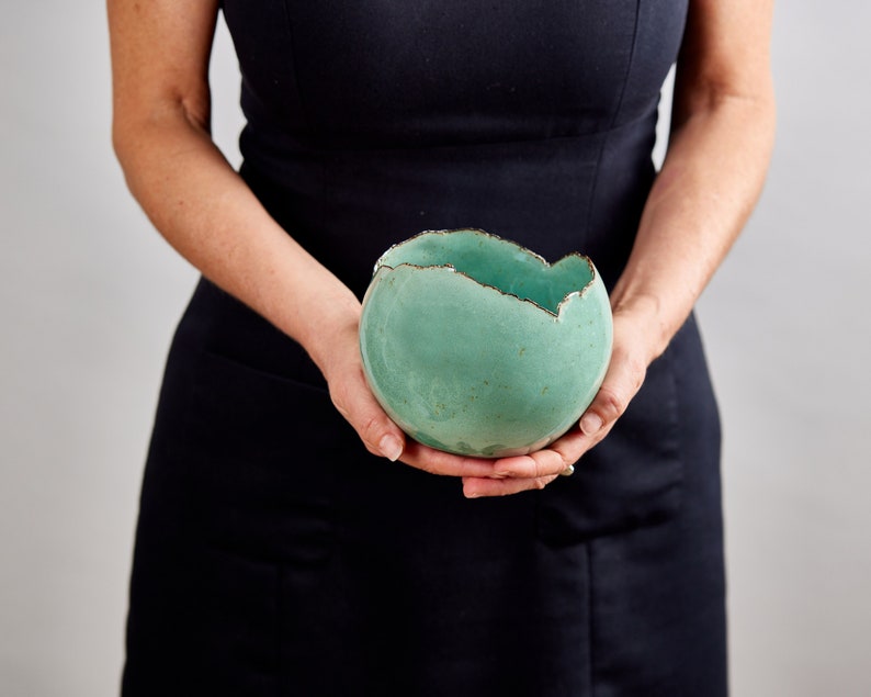 May include: A teal ceramic bowl with a rough, uneven rim. The bowl is slightly misshapen and has a rustic, handmade look.