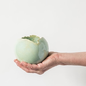 Può includere: Una ciotola in ceramica verde chiaro con un bordo scheggiato, tenuta in una mano.