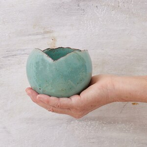 May include: A small, teal-colored ceramic planter with a rough, textured surface. The planter has an uneven, slightly jagged rim.