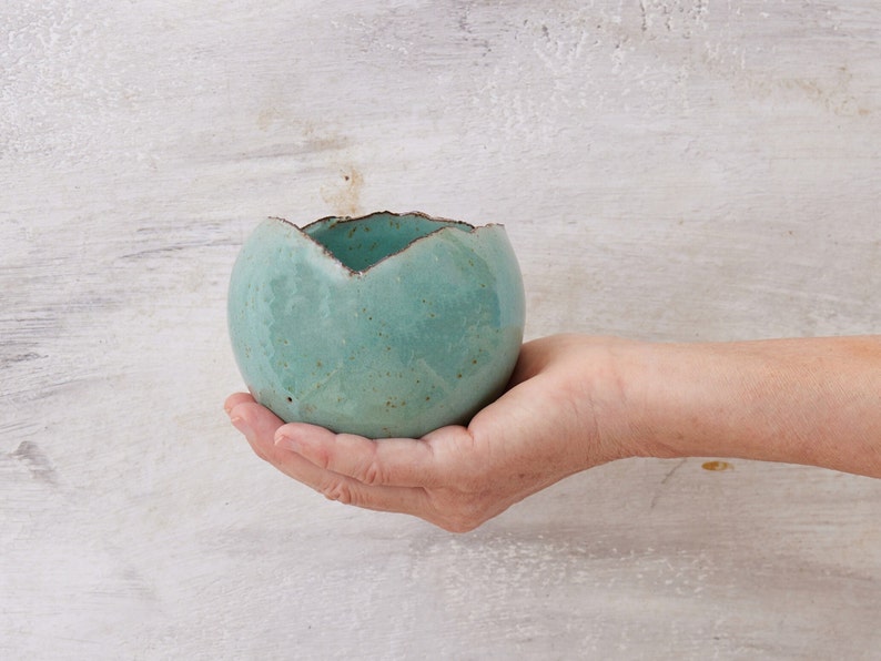May include: A small, teal-colored ceramic planter with a rough, textured surface. The planter has an uneven, slightly jagged rim.