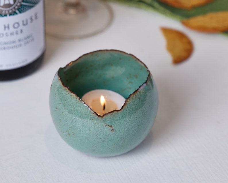 May include: Teal ceramic candle holder with a rough, textured exterior and a small white tea light candle inside.