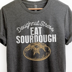 May include: A dark gray t-shirt with a white graphic that says "Doughnut Stress Eat Sourdough" with a drawing of a sourdough loaf of bread.