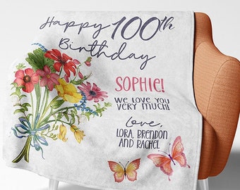 Op de afbeelding: Een witte deken met een bloemenpatroon en de tekst "Happy 100th Birthday Sophie! We love you very much! Love, Lora, Brendon and Rachel".