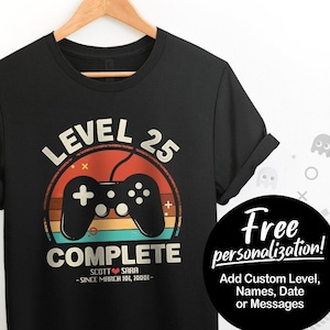 May include: Black t-shirt with a retro-style video game controller graphic and the text "Level 25 Complete". The graphic has a rainbow color scheme. The text "Scott Sara - Since March 18, 1988" is below the graphic.