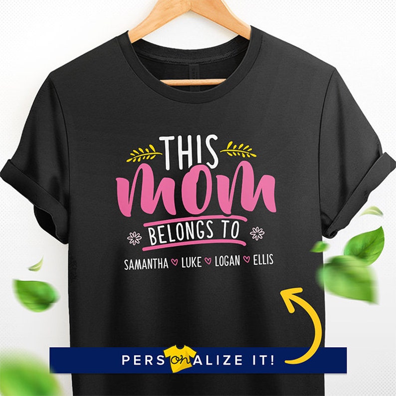 K&ouml;nnte beinhalten: Schwarzes T-Shirt mit dem Text "This Mom Belongs To" in Pink und Gelb. Unter dem Text stehen die Namen Samantha, Luke, Logan und Ellis, getrennt durch Herzen.
