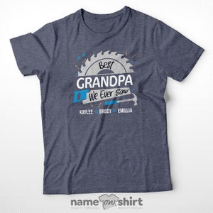 Pu&ograve; includere: Una maglietta blu con una grafica a forma di lama da sega bianca che dice "Best Grandpa We Ever Saw" con i nomi Kaylee, Brody ed Emillia sotto. La maglietta &egrave; della societ&agrave; "name on shirt".