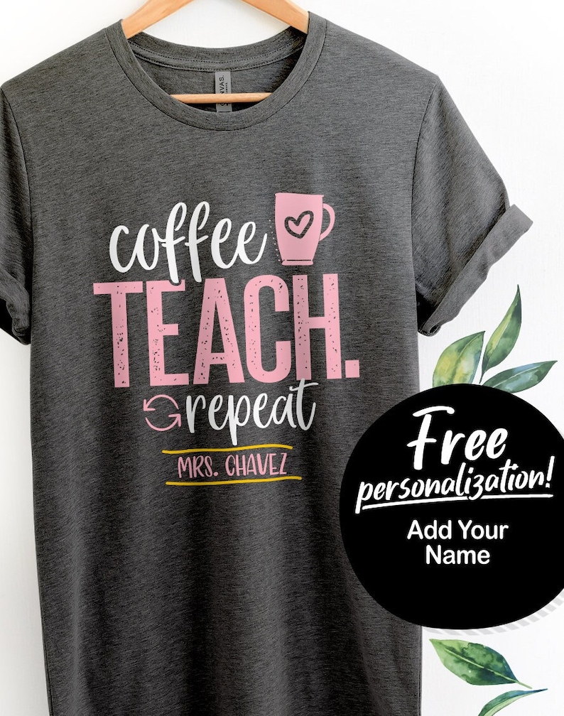 May include: Gray t-shirt with the text "coffee teach repeat" in pink and white. A pink coffee cup with a heart is above the text. The text "MRS. CHAVEZ" is below the text in yellow. A black circle with white text says "Free personalization! Add Your Name".