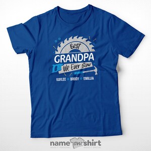 Pu&ograve; includere: Maglietta blu con una grafica di lama da sega bianca che dice "Best Grandpa We Ever Saw" con i nomi Kaylee, Brody ed Emillia sotto.