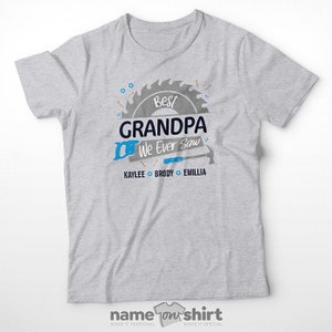 Pu&ograve; includere: Maglietta grigia con un design a lama di sega e il testo "Best Grandpa We Ever Saw" con i nomi Kaylee, Brody ed Emillia sotto.