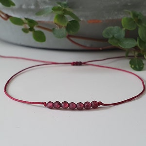 Könnte beinhalten: Ein rotes Armband mit einer Reihe kleiner, dunkelroter Edelsteinperlen.