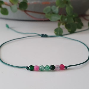 May include: A green string bracelet with a row of small green, pink and purple beads.