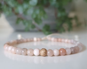Könnte beinhalten: Ein zartes Armband aus rosa und weißen Perlen mit einer goldenen Perle mit strukturierter Oberfläche.