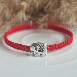 Peut inclure: Bracelet en cordon rouge avec un charme d'éléphant argenté. Le bracelet est fait de cordon tressé et le charme est détaillé avec une surface texturée.