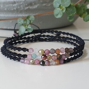 May include: A multi-colored gemstone bracelet with pink, green, and brown beads on a black cord.