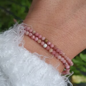 Puede incluir: Un brazalete de doble cadena hecho de cuentas rosadas con un acento de cuentas doradas y plateadas.