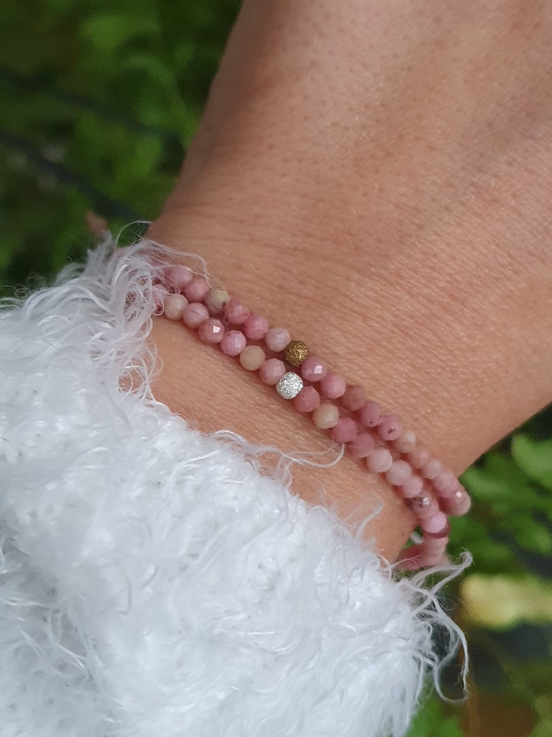 Puede incluir: Un brazalete de doble cadena hecho de cuentas rosadas con un acento de cuentas doradas y plateadas.