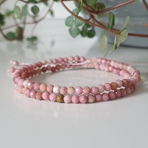 Puede incluir: Un brazalete de piedras preciosas rosas con detalles plateados y dorados. El brazalete est&aacute; hecho de peque&ntilde;as cuentas facetadas y est&aacute; en capas en una doble hebra.