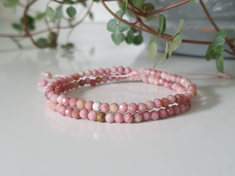 Puede incluir: Un brazalete de piedras preciosas rosas con detalles plateados y dorados. El brazalete est&aacute; hecho de peque&ntilde;as cuentas facetadas y est&aacute; en capas en una doble hebra.