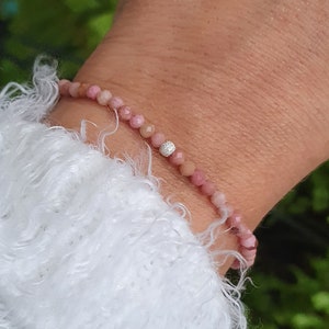 Puede incluir: Un brazalete de piedras preciosas rosas con un solo acento de diamante. El brazalete est&aacute; hecho de peque&ntilde;as cuentas redondas y se lleva en la mu&ntilde;eca.