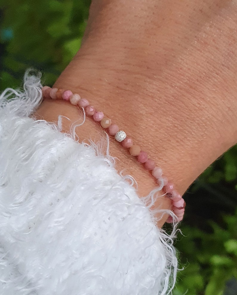 Puede incluir: Un brazalete de piedras preciosas rosas con un solo acento de diamante. El brazalete est&aacute; hecho de peque&ntilde;as cuentas redondas y se lleva en la mu&ntilde;eca.