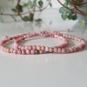 Puede incluir: Dos pulseras de piedras preciosas rosas con un acento de cuentas doradas y plateadas. Las pulseras est&aacute;n hechas de peque&ntilde;as cuentas facetadas y est&aacute;n atadas juntas con un hilo delgado.
