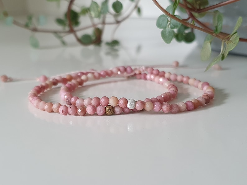 Puede incluir: Dos pulseras de piedras preciosas rosas con un acento de cuentas doradas y plateadas. Las pulseras est&aacute;n hechas de peque&ntilde;as cuentas facetadas y est&aacute;n atadas juntas con un hilo delgado.