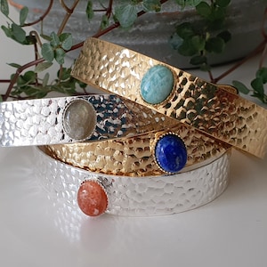Puede incluir: Cuatro pulseras de oro y plata con piedras preciosas de diferentes colores. Las pulseras están apiladas una encima de la otra. Las piedras preciosas son azul claro, azul oscuro, verde y naranja.