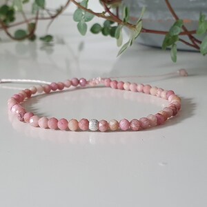 Puede incluir: Un brazalete de piedras preciosas rosas con un acento de cuentas plateadas. El brazalete est&aacute; hecho de peque&ntilde;as cuentas redondas y est&aacute; atado con un hilo delgado.