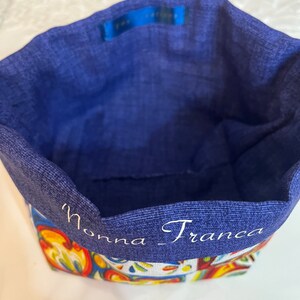 Può includere: Un cestino di stoffa blu con un motivo floreale colorato alla base e un interno blu tinta unita. Le parole "Nonna_Franca" sono ricamate in bianco sul bordo.