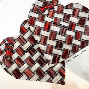 Può includere: Due decorazioni a forma di cuore con un motivo intrecciato rosso, bianco e bordeaux. Ogni cuore ha un piccolo fiocco a quadri e la parola "GORGEOUS" stampata sopra. È visibile anche il testo "EMY CREATIONS".
