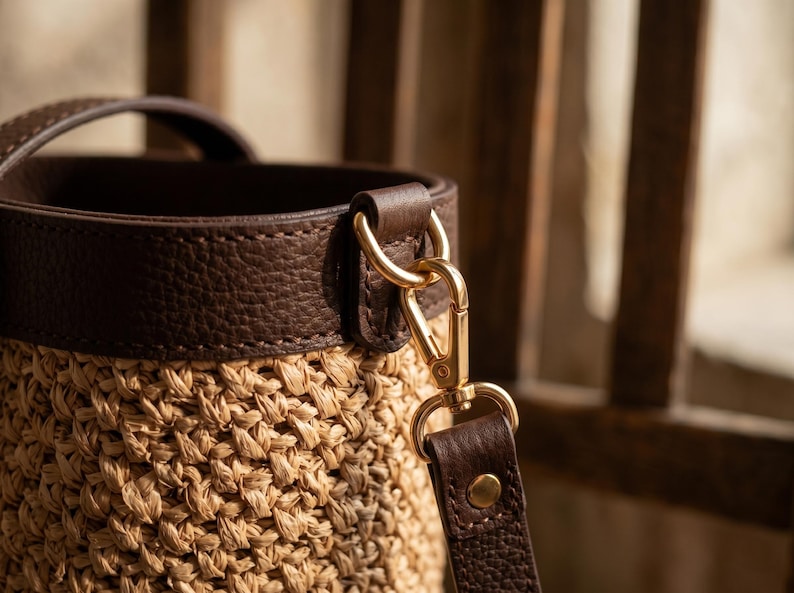 May include: A bucket bag featuring a woven tan straw body and a dark brown pebbled leather top trim. The bag includes a dark brown leather handle and a detachable dark brown leather shoulder strap connected by polished gold-tone metal hardware.