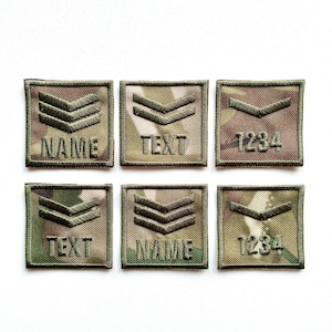 Peut inclure: Six écussons de camouflage carrés avec des chevrons brodés et du texte. Les écussons comportent les mots "NAME", "TEXT" et les chiffres "1234". Les écussons ont une bordure verte.