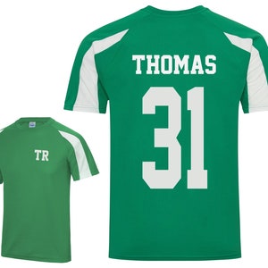 May include: Two green athletic shirts with white accents. One shirt has the initials "TR" on the front. The other shirt has the name "THOMAS" and the number "31" on the back. Both shirts have white shoulder panels.