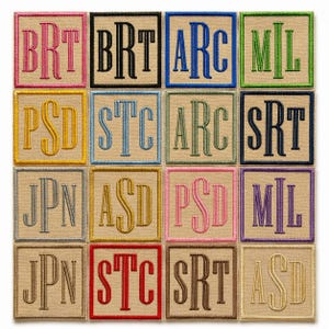 May include: Sixteen square embroidered patches with three-letter monograms. Each patch has a different coloured border and monogram, including pink, black, blue, green, yellow, light blue, and purple. The patches are on a neutral background.