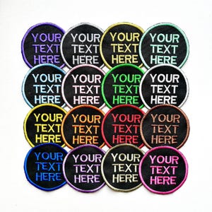 May include: A selection of embroidered patches, each featuring the text "YOUR TEXT HERE" in different colours, such as purple, white, yellow, and green. The patches have a black background and a coloured border. The round patches are arranged in a grid.