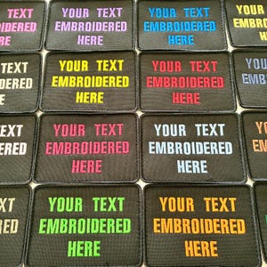 May include: A selection of black, rectangular embroidered patches. Each patch displays the text "YOUR TEXT EMBROIDERED HERE" in a range of colours, such as purple, blue, yellow, red, and green. The patches are arranged in a grid.
