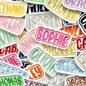 May include: A selection of embroidered name patches in different colours and fonts. Names such as Sophie, Olivia, and Amelia are visible. Each patch has a white background with colourful stitching.