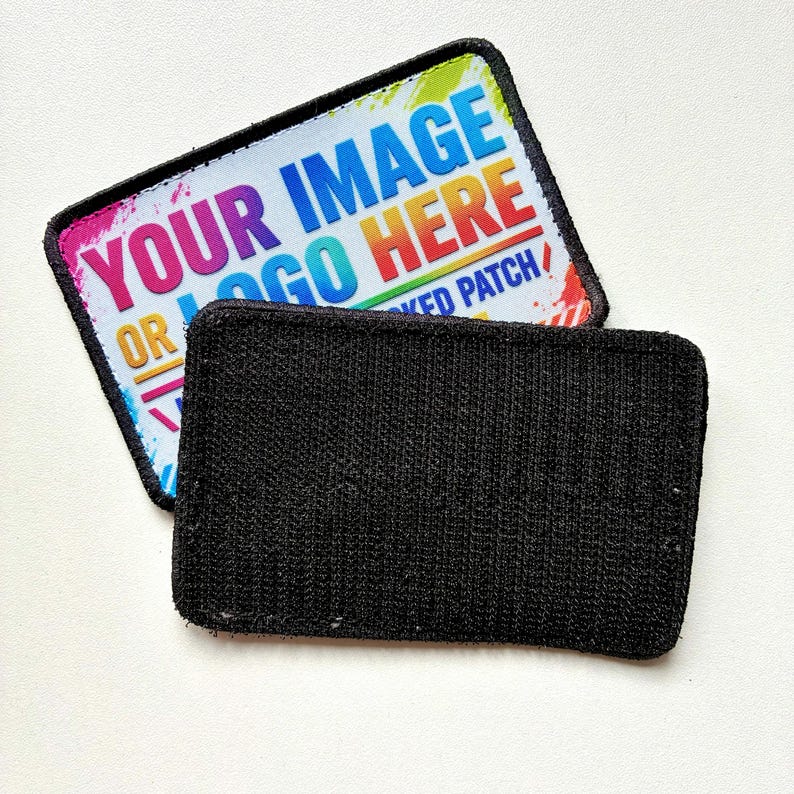 K&ouml;nnte beinhalten: Zwei rechteckige Aufn&auml;her mit abgerundeten Ecken. Der obere Aufn&auml;her hat einen wei&szlig;en Hintergrund mit einem bunten Regenbogenverlauf und dem Text "YOUR IMAGE OR LOGO HERE" in fetten blauen und roten Buchstaben. Der untere Aufn&auml;her ist schwarz mit Klettverschluss.
