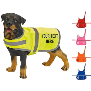 May include: A black and brown dog wearing a bright yellow safety vest with reflective strips. The vest has the text "YOUR TEXT HERE" printed on it. The image also shows four different colored vests in the background: red, pink, orange, and blue.