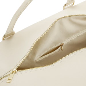 May include: A cream-colored leather tote bag with a gold zipper and a small interior pocket. The bag has a top handle and a zipper closure.