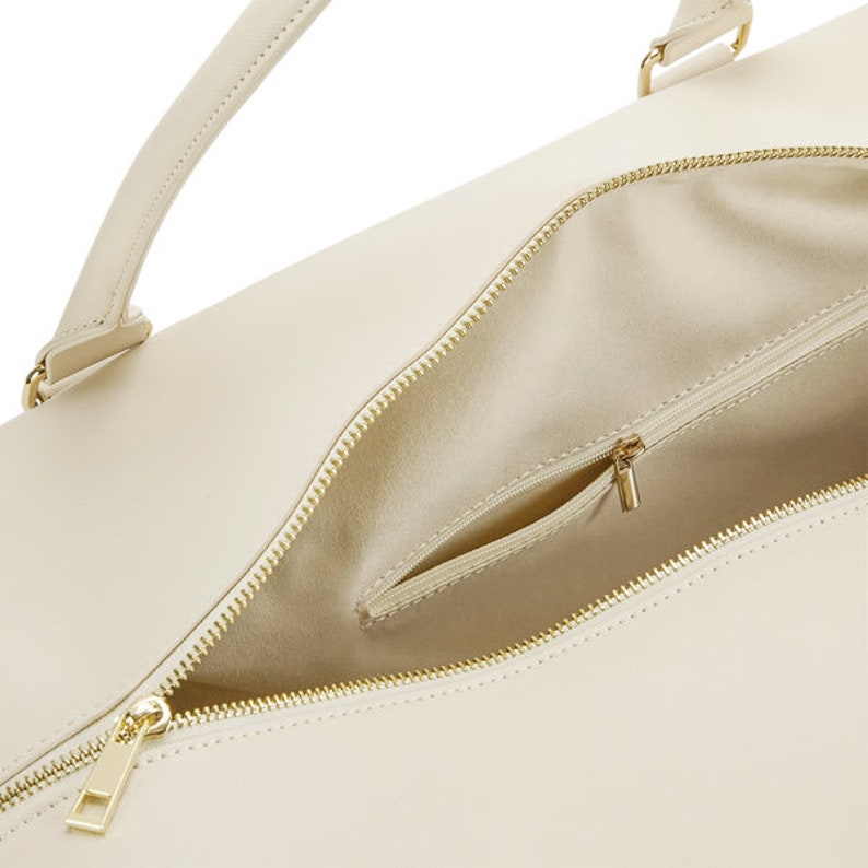 May include: A cream-colored leather tote bag with a gold zipper and a small interior pocket. The bag has a top handle and a zipper closure.